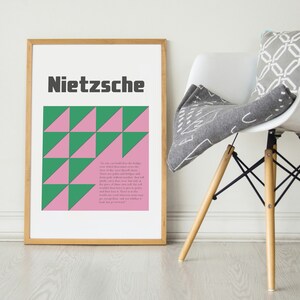May include: A framed print with a geometric pattern of pink and green triangles. The print features the word "Nietzsche" in black text at the top and a quote from Nietzsche in smaller text below the pattern.