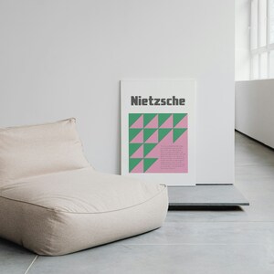 May include: A beige bean bag chair sits in a minimalist room with a white wall and a poster with the word "Nietzsche" and a geometric pattern of green and pink triangles.