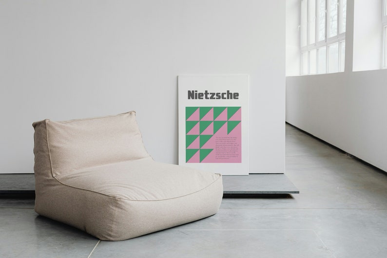 May include: A beige bean bag chair sits in a minimalist room with a white wall and a poster with the word "Nietzsche" and a geometric pattern of green and pink triangles.