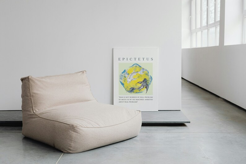 May include: A beige bean bag chair sits in front of a white wall with a poster featuring a quote by Epictetus. The poster has a light green background with a yellow and blue abstract design.