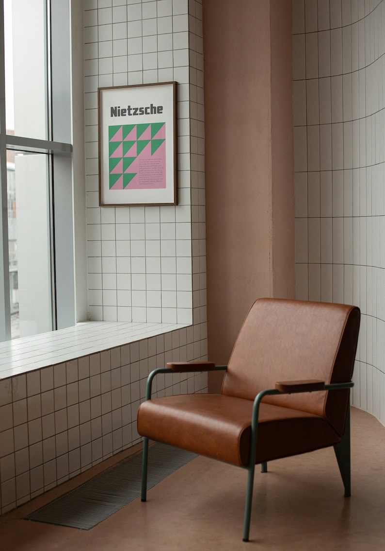 May include: A brown leather armchair with a metal frame sits in a room with white tiled walls. A framed poster with the word "Nietzsche" and a geometric design hangs on the wall.