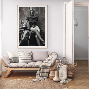 May include: A black and white photograph of a woman wearing sunglasses and a scarf sitting on a vintage scooter.