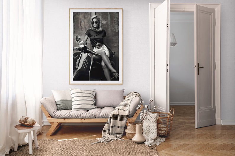 May include: A black and white photograph of a woman wearing sunglasses and a scarf sitting on a vintage scooter.