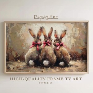 May include: Painting of three brown rabbits with pink bows, standing in a field of tall grass. The painting is framed in a light wood frame.