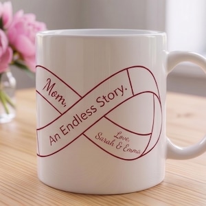 May include: White ceramic mug with a burgundy infinity symbol design and the words "Mom, An Endless Story. Love, Sarah & Emma." A gift box and pink peonies are in the background. A perfect gift for Mother's Day.