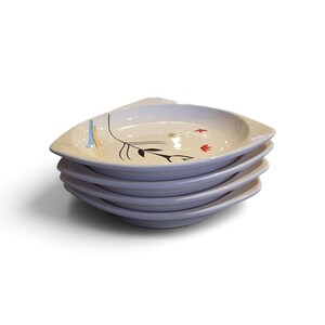 May include: A stack of four white ceramic plates with a rounded triangular shape. Each plate features a black line drawing of a stylized flower stem with small red and blue accents on the surface. The plates have a smooth, glossy finish.