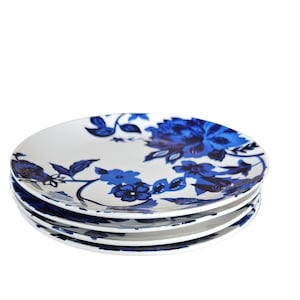 Puede incluir: Una pila de cuatro platos de cerámica blancos con un diseño floral azul. Los platos presentan un patrón repetido de flores grandes y pequeñas y hojas en tonos azules. Los platos están apilados unos sobre otros.