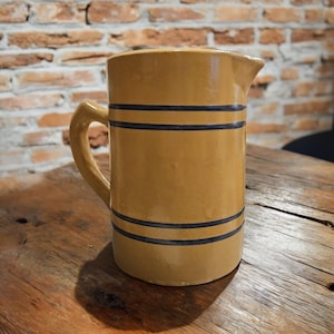 Könnte beinhalten: Ein gelber Keramik-Krug mit einem blauen Streifenmuster. Der Krug hat einen Henkel und einen Ausguss.