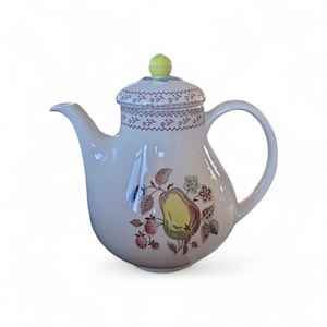 May include: Cream ceramic teapot with a pear and floral design. The teapot has a curved spout, rounded body, and a handle. The lid features a yellow knob and a decorative border. The design includes pears, flowers, and berries. A charming addition to any kitchen.