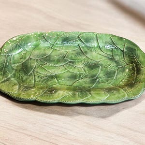 Puede incluir: Un plato de servir de cerámica verde con un diseño de hojas. El plato es de forma ovalada y tiene un acabado brillante.
