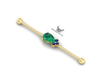 May include: Gold barbell with a teardrop-shaped emerald gemstone and four smaller blue gemstones.