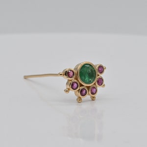 May include: A gold nose ring with a green emerald gemstone surrounded by smaller pink gemstones.