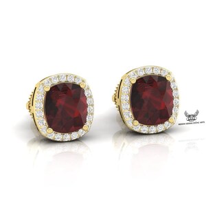 Peut inclure: Une paire de boucles d'oreilles en or avec une pierre précieuse rouge entourée d'un halo de petites pierres blanches.