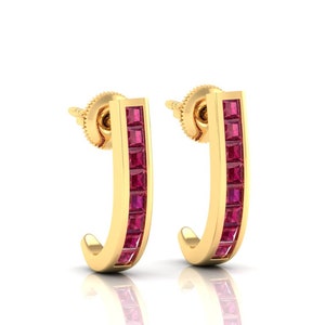 Pode incluir: Um par de brincos de argola de ouro com uma fileira de pedras quadradas vermelhas.