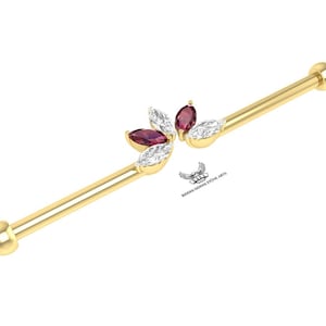 May include: A gold-colored industrial barbell earring with a floral design. The flower has five marquise-cut gemstones, alternating between clear and deep red. The barbell has rounded ends.