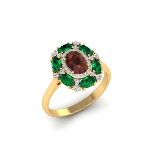 Peut inclure: Une bague en or avec une pierre centrale ovale brun-rouge, entourée de pierres vertes en forme de marquise et de petits gemmes blancs. Le corps de la bague est de couleur or poli.