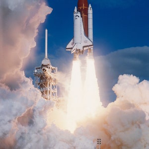 Op de afbeelding: Een witte en rode spaceshuttle lanceert de lucht in, en laat een spoor van witte rook en vuur achter. De shuttle wordt omringd door wolken.