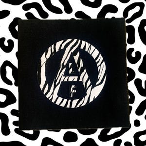 Könnte beinhalten: Schwarz-weißer Aufkleber mit einem Zebra-Kreis, der die Buchstaben "AF" in einem weißen Dreieck enthält.