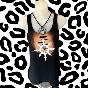 Könnte beinhalten: Schwarzes Tanktop mit einem weißen und beigefarbenen Sternenmuster. Das Oberteil hat einen gebleichten Effekt über der Brust und eine schwarze Halskette mit Anhänger. Der Hintergrund ist ein schwarz-weißer Leopardenmusterdruck.