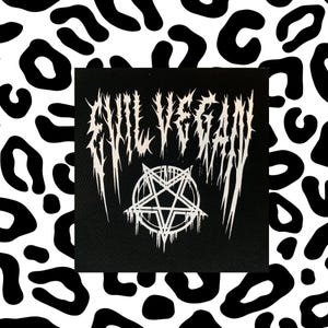 Könnte beinhalten: Schwarzer Patch mit weißem Text, der in gotischer Schrift "Evil Vegan" lautet. Ein weißes Pentagramm mit tropfenden Kanten ist mittig unter dem Text platziert.