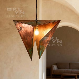 Puede incluir: Una lámpara colgante geométrica de color cobre con forma triangular, suspendida de un soporte de techo de madera. La lámpara emite un brillo cálido. La habitación incluye una mesa de comedor y sillas de madera.