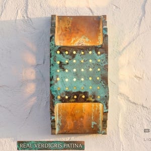 Könnte beinhalten: Rechteckige Wandleuchte mit Kupferfinish und türkisfarbener Verdigris-Patina. Die Leuchte hat kleine, gleichmäßig verteilte goldfarbene Punkte. Der Text "REAL VERDIGRIS PATINA" steht darunter.