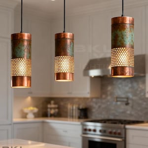 May include: Three copper-finished cylindrical pendant lights with a perforated lower section and a teal patina on the upper part. They hang from black cords in a kitchen. The brand name "BKL YN LIGHTING" is visible.