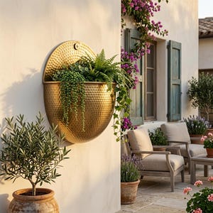 Peut inclure: Une jardinière murale semi-circulaire en métal doré martelé. La jardinière présente une plaque arrière plate et un bol arrondi, contenant une variété de plantes vertes retombantes, notamment des fougères et des séneçons à chapelets.