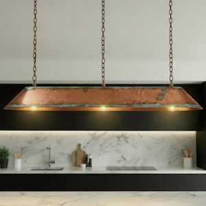 May include: A rectangular copper pendant light fixture with three bulbs, suspended by chains. The fixture has a weathered, aged appearance with hints of turquoise. The light is installed in a kitchen setting.