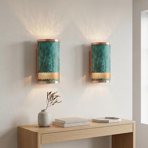 May include: Two wall sconces with a cylindrical design. The sconces feature a teal, textured finish with copper-colored trim and a perforated band at the bottom. They are mounted on wooden backplates, casting a warm light.