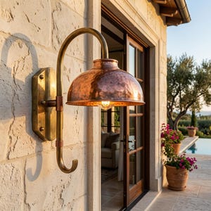 May include: Outdoor wall-mounted light fixture with a copper shade and brass arm. The fixture is mounted on a textured stone wall. The light has a curved arm and a hook at the bottom.