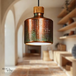 Puede incluir: Una lámpara colgante de color cobre con una parte superior de madera y una pantalla de metal perforada. La lámpara está suspendida de un cable negro y emite un brillo cálido. El texto "BKL YN LIGHTING" es visible en la parte inferior.