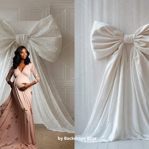May include: A white backdrop with a large white bow made of fabric. A pregnant person is standing in front of the backdrop wearing a long, pink dress.