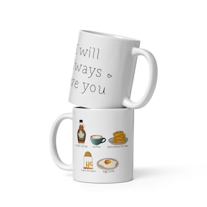 May include: Two white ceramic mugs, one stacked on top of the other. The top mug has the text "I will always love you" in black. The bottom mug has illustrations of maple syrup, coffee, pancakes, hash browns, and an egg yolk.