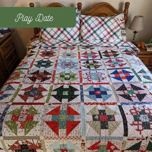 May include: A handmade quilt with a patchwork design featuring squares of various colours and patterns, including red, green, blue, and white. The quilt is on a bed with matching plaid pillowcases. The text "Play Date" and "Scrap Basket Quilts" are visible.