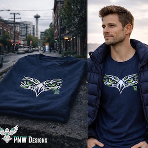 May include: Navy blue t-shirt featuring a stylized eagle eye design in white, green, and black. The number "12" is printed in green. The shirt is displayed on a stone surface and worn by a person.
