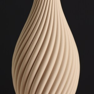 May include: A beige ceramic vase with a unique, swirling, textured design. The vase has a rounded, bulbous shape.