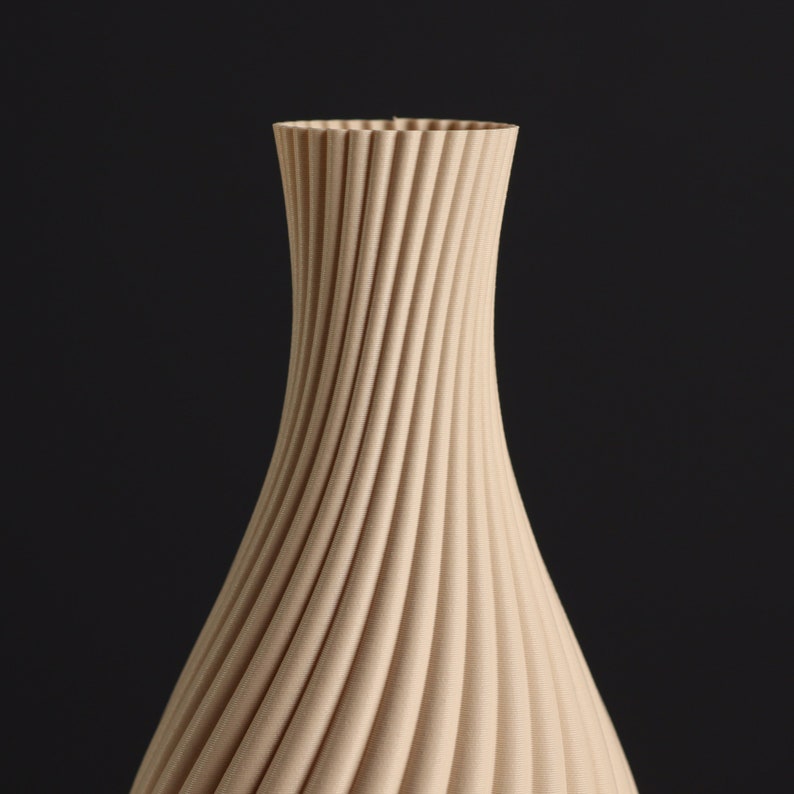 May include: A beige ceramic vase with a unique, swirling, ribbed design. The vase is tall and slender, with a narrow opening at the top.