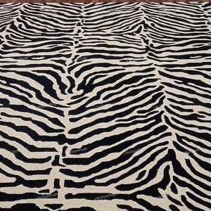 Puede incluir: Una alfombra grande con un patrón de rayas de cebra de alto contraste en negro y blanco roto. El diseño consiste en líneas onduladas, orgánicas y repetitivas que cubren toda la superficie del revestimiento rectangular para el suelo.
