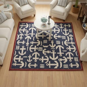 May include: A navy blue area rug with a nautical anchor pattern in cream. The rug has a red border and is surrounded by white furniture. The room has a coastal theme.