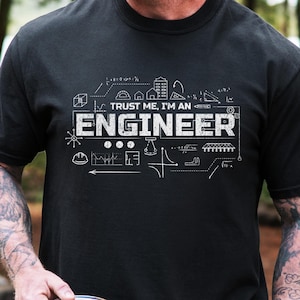 May include: Black t-shirt featuring the text "TRUST ME, I'M AN ENGINEER" in white, along with engineering diagrams. The short-sleeved shirt is made of a soft fabric. The design is printed on the front.