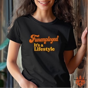 May include: Black t-shirt with the text "Funemployed It's a Lifestyle" in orange and yellow retro font. The shirt is a short-sleeved crew neck style. The brand name "WOODSY WEARABLES" is printed at the bottom right.