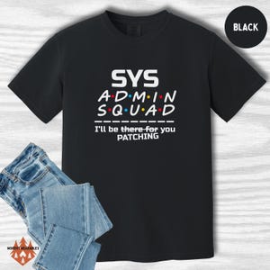 May include: Black t-shirt with the text "SYS ADMIN SQUAD" in white, with coloured dots. Below the text is "I'll be there for you PATCHING". A pair of blue jeans is folded below the shirt. A black circle with the word "BLACK" is in the upper right corner.
