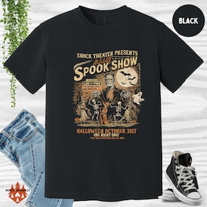 May include: Black t-shirt featuring a vintage Halloween illustration of Frankenstein's monster, skeletons, and a ghost. The text reads "Shock Theater Presents Annual Spook Show" and "Halloween October 31st One Night Only".
