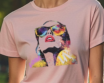 Puede incluir: Una camiseta rosa claro con un gráfico colorido de una mujer con gafas de sol. El gráfico es de estilo pop art con colores vibrantes. La mujer está mirando hacia arriba, y la palabra "cool" está escrita en rosa en la camiseta.