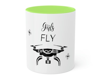 May include: White ceramic mug with a green rim. The mug has a black drone graphic and the text "Girls FLY DRONES" printed on it.