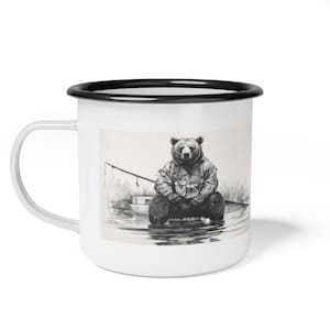 Può includere: Una tazza di smalto bianco con un bordo nero presenta un'illustrazione in bianco e nero di un orso che indossa una camicia a quadri e siede in una piccola barca con una canna da pesca. L'orso guarda direttamente lo spettatore.