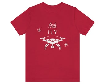 May include: Red t-shirt with white text that says "Girls Fly" and a white silhouette of a drone with the word "DRONES" printed on it.