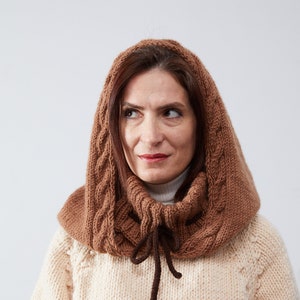 May include: A brown knitted cowl with a cable knit pattern and a tie at the neck. The cowl is worn by a person with brown hair.