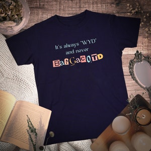 Op de afbeelding: Een marineblauw t-shirt met de tekst "It's always 'WYD' and never BagGaCoTD" gedrukt in kleurrijke letters.